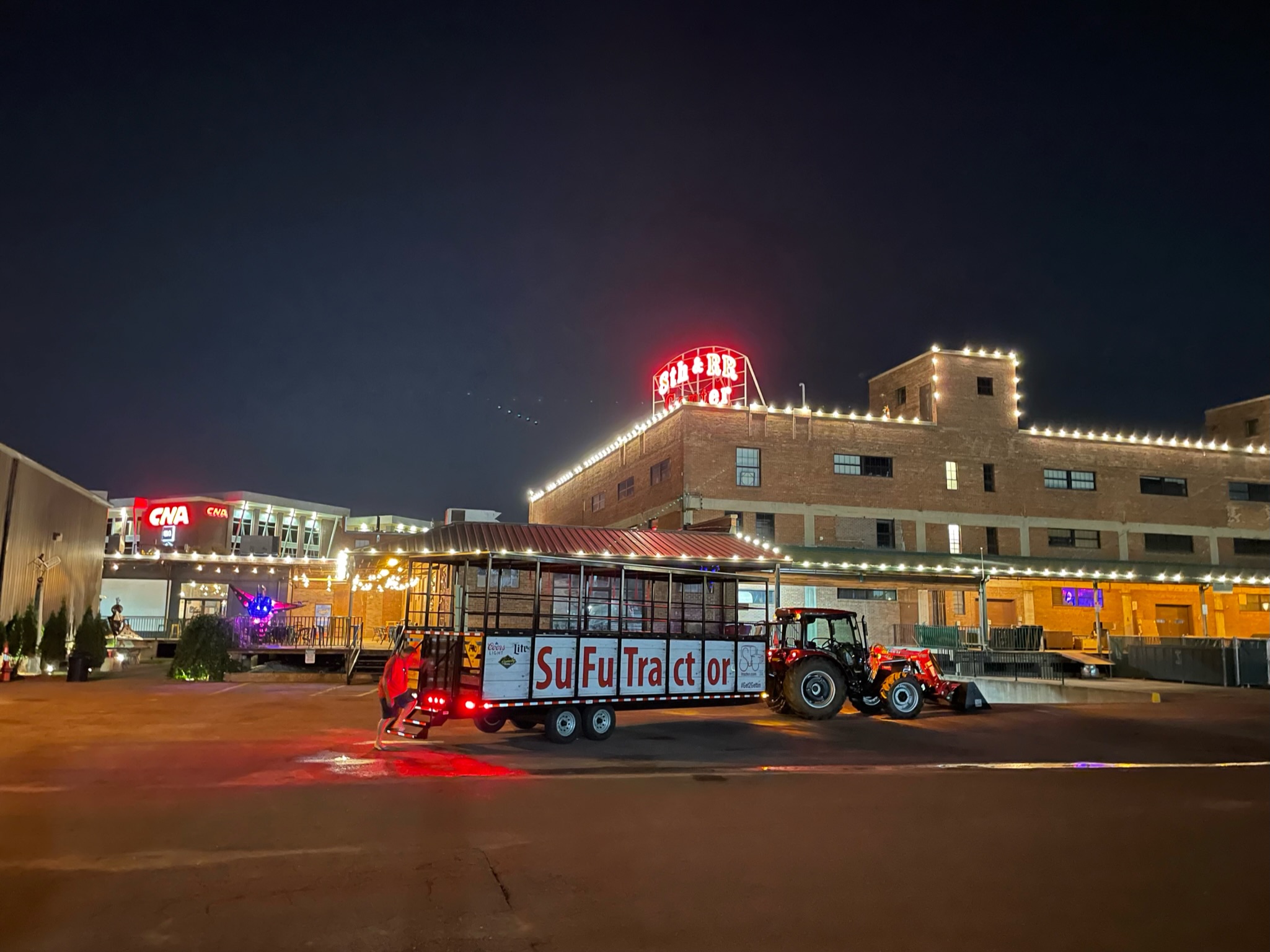 SuFuTractor wagon lit up at night outside the historic 8th & RR Center brick building with string lights in downtown Sioux Falls
