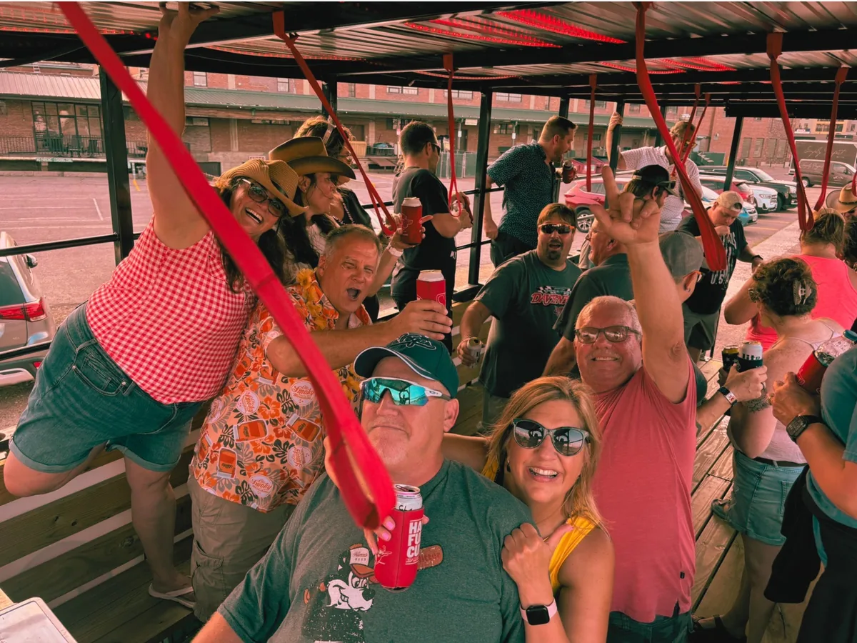 Large group of adults celebrating on the SuFu Tractor party wagon during a daytime ride in Sioux Falls